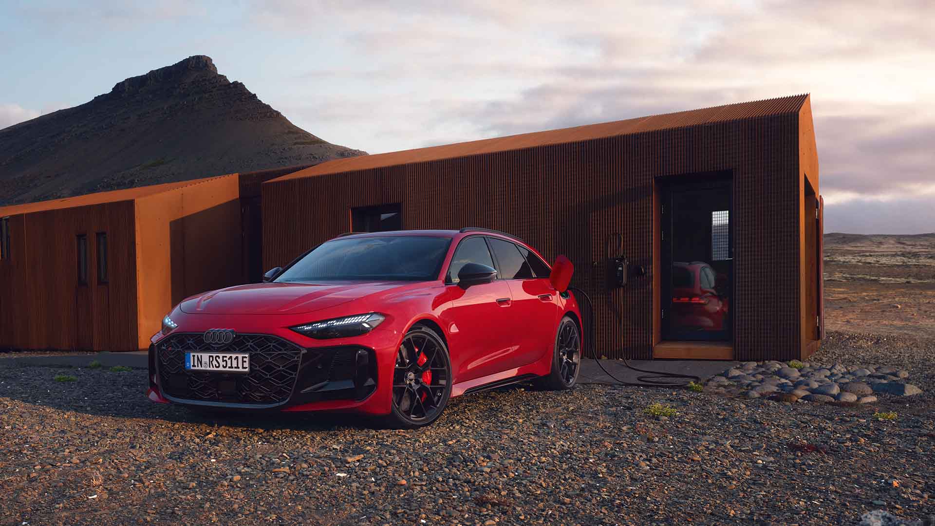 Audi RS 5 Avant, rot, Frontansicht, stehend an Ladesäule vor einem mordernen Holzhaus