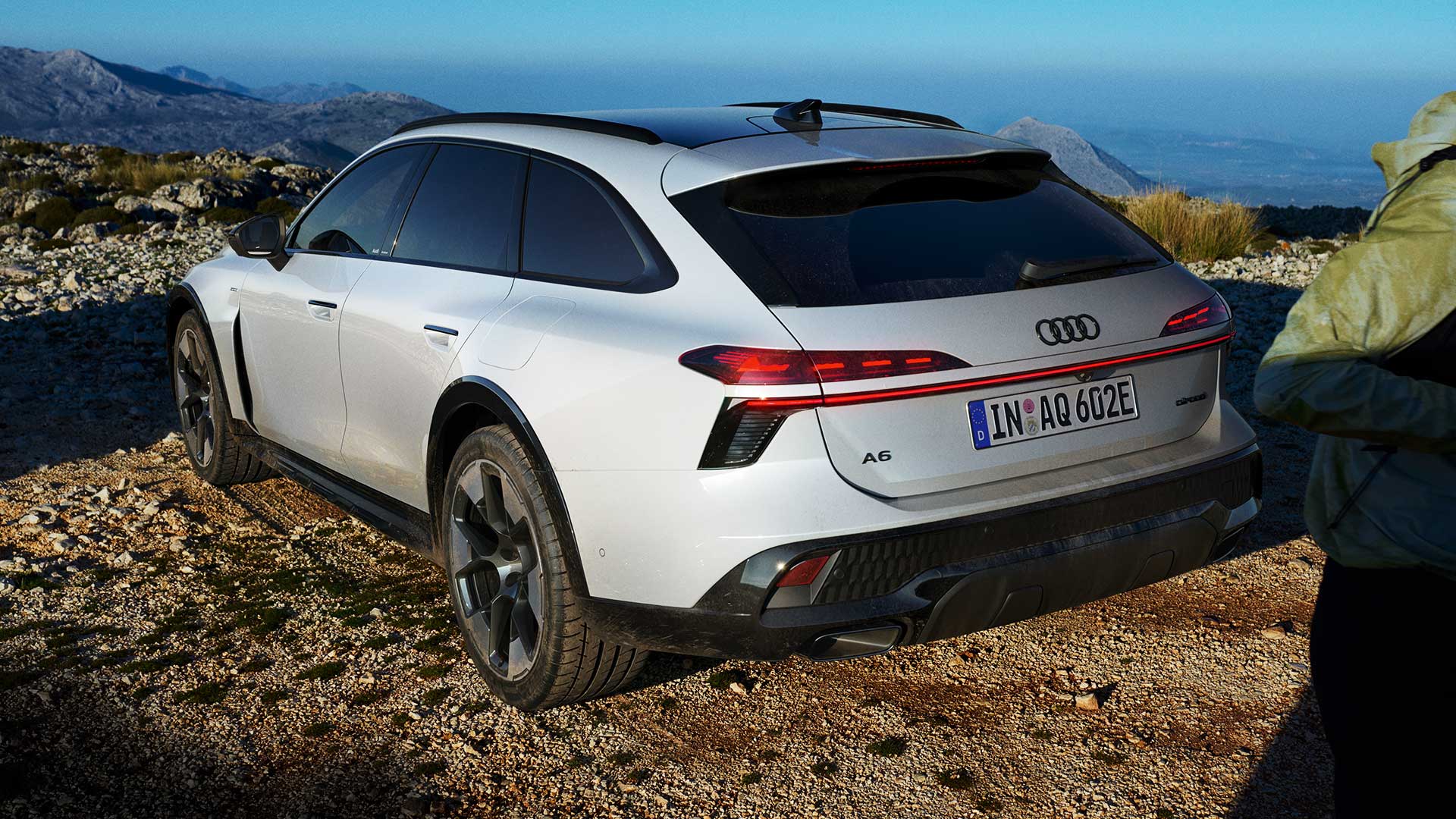 Audi A6 allroad e-hybrid, weiß, Heckansicht, stehend auf unbefestigtem Untergrund